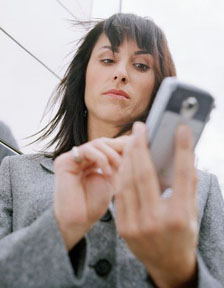 Business woman standing outside in front of office building, using mobile phone --- Image by © Royalty-Free/Corbis