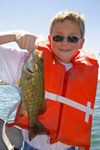 A twelve year old boy wearing a life jacket and holding a bass he caught while fishing in Idaho. MR