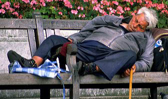 A homeless man sleeps on a park bench in London, England.